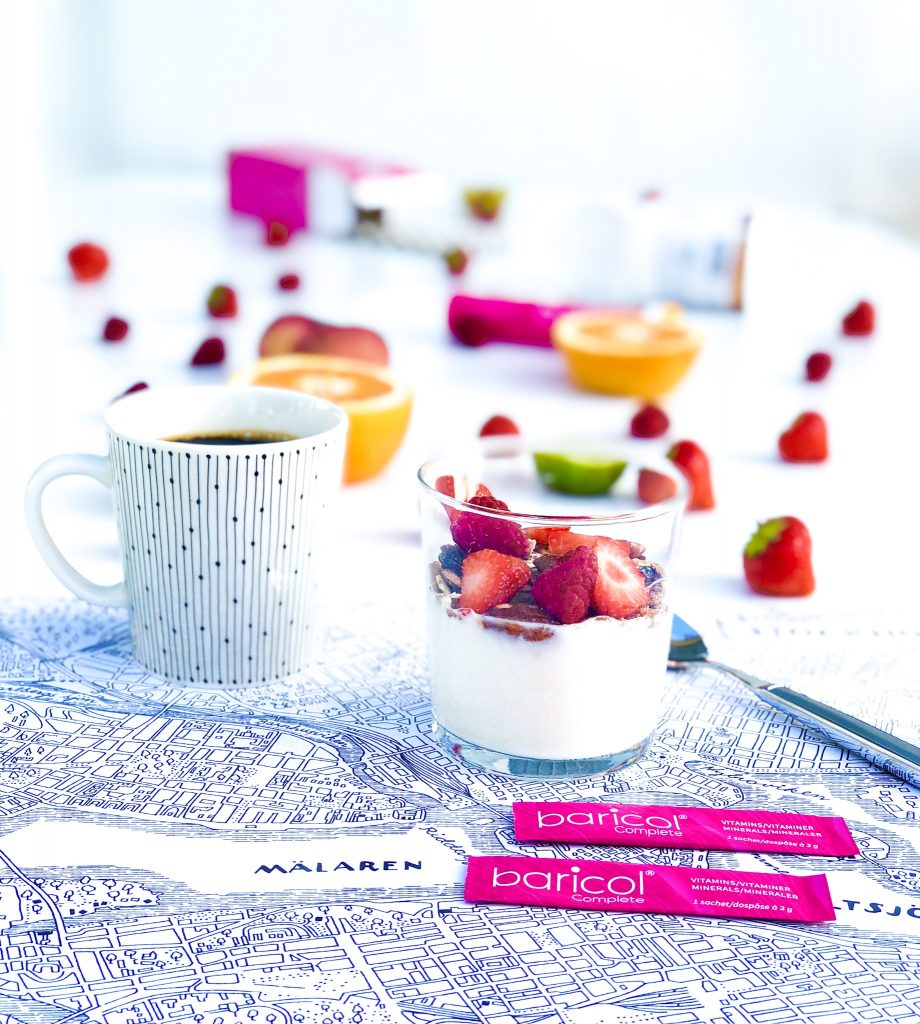 Frukostunderlägg med stockholmskarta på den står kaffekopp, glas med yoghurt med granola och jordgubbar omgiven av två dospåsar baricol pulver